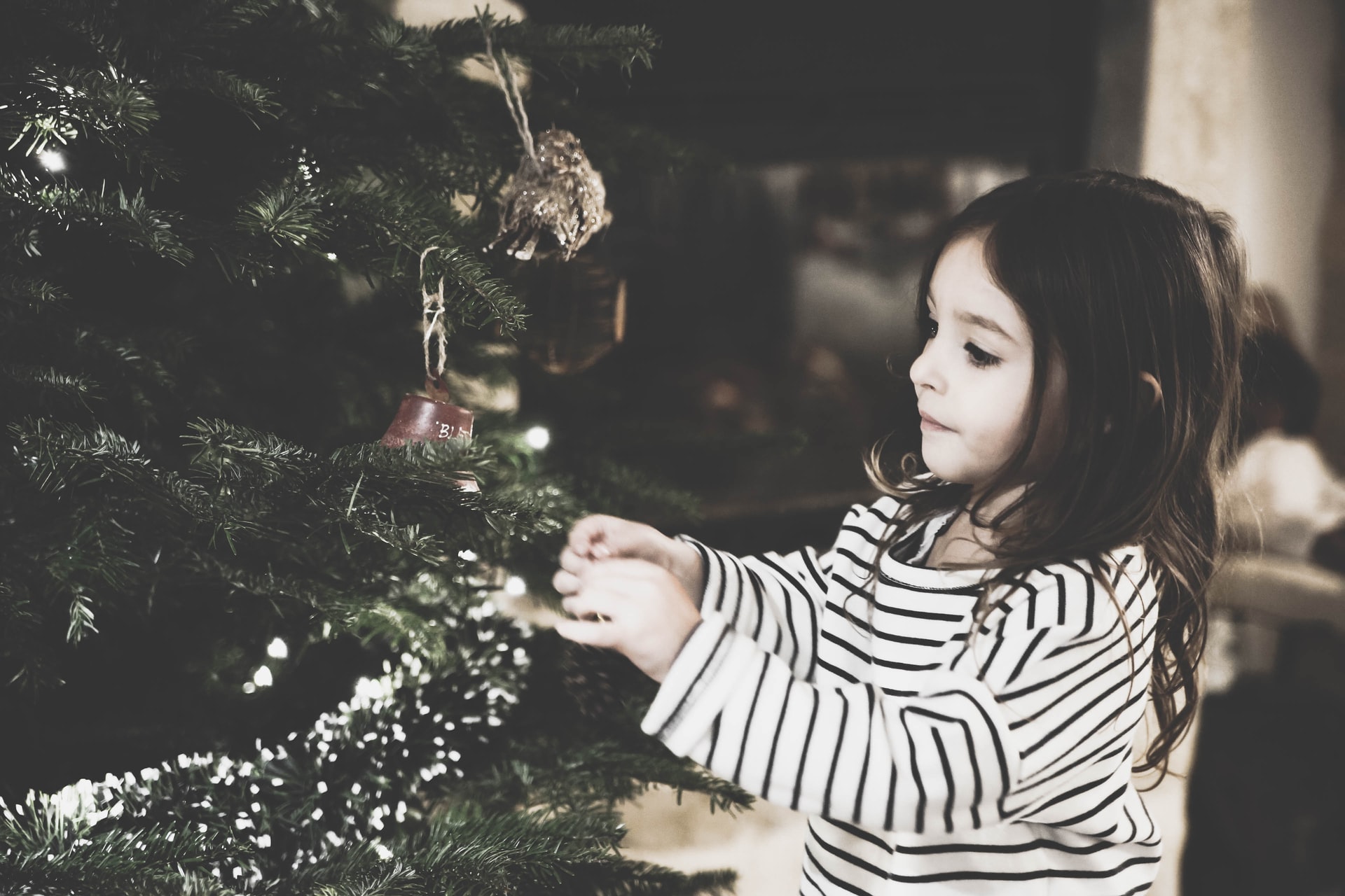a little girl decorating the Christmas tree to represent how to be happy this christmas